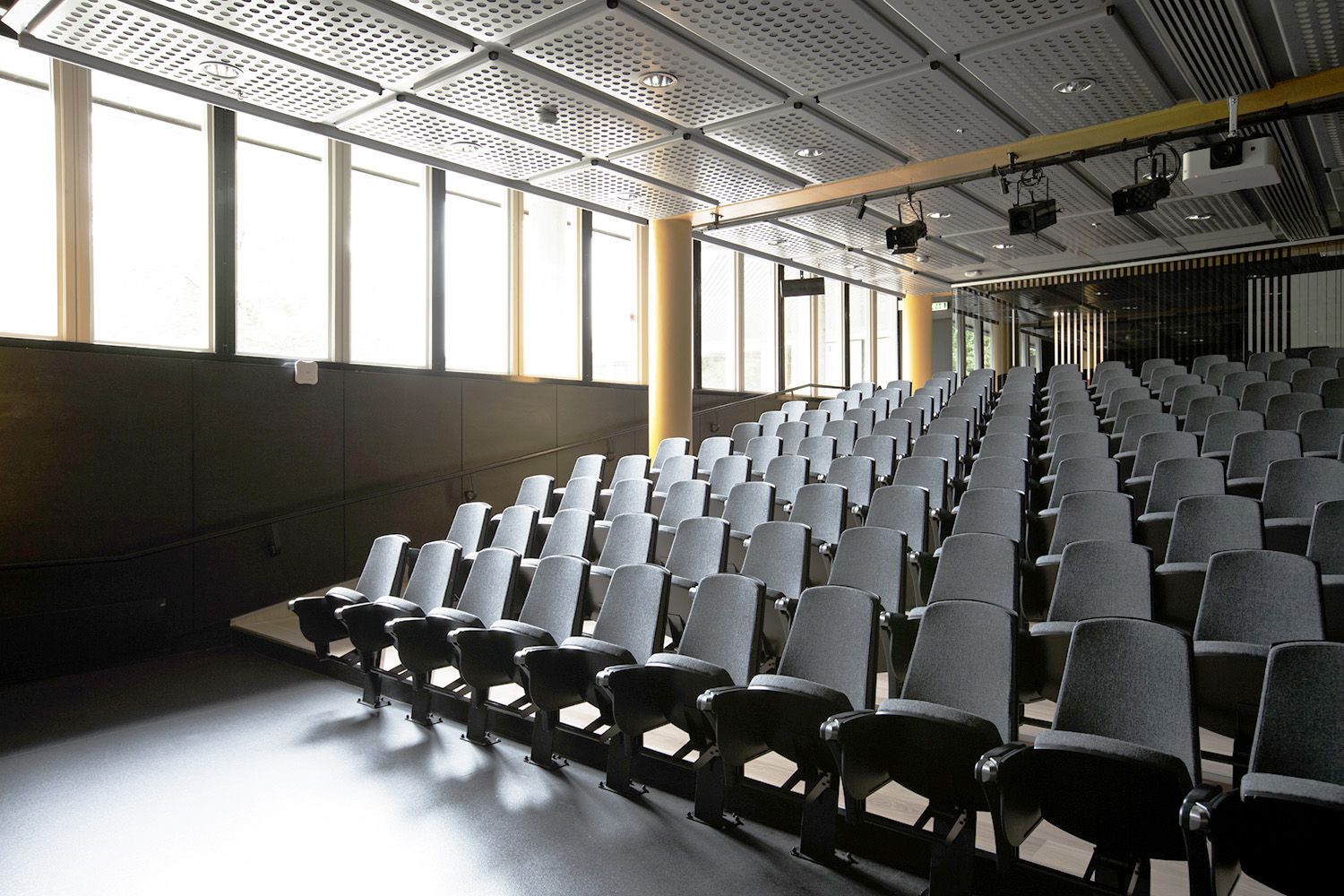 Auditorium med stolrader, dagslys og gule søyler.