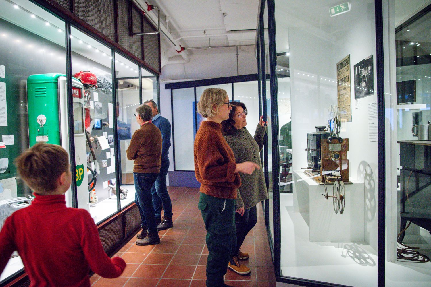 Et barn og voksne ser på gjenstander i montere
