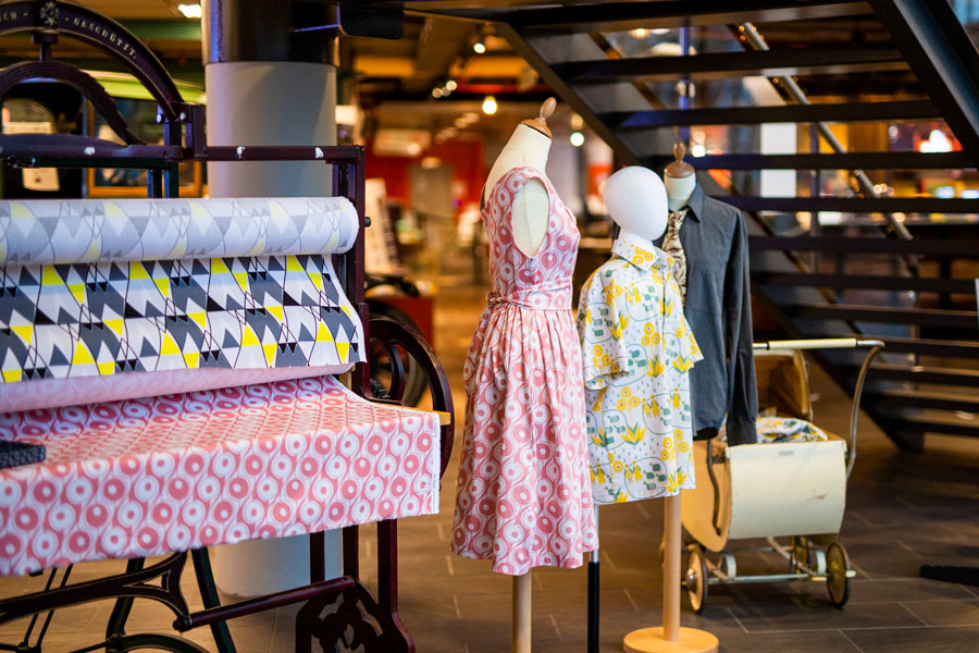 Ruller med stoff og to klesplagg laget av samme stoffet hengt opp på mannekeng.