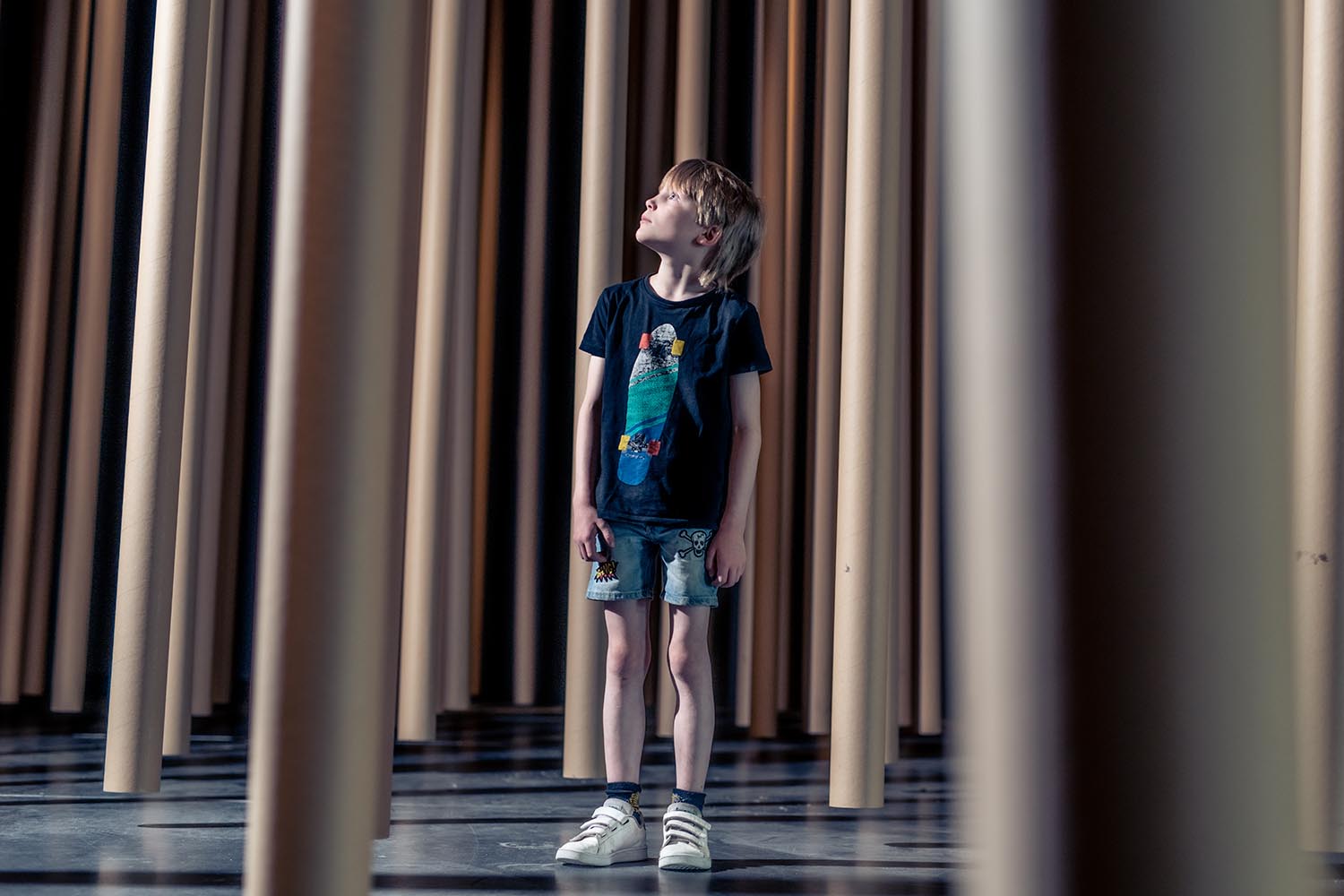 Liten gutt i midten av mange papprør hengende fra taket.