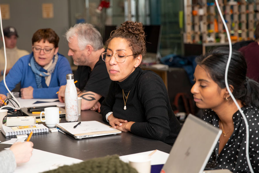Fire voksne mennesker sitter ved et langbord med pc og notatblokker