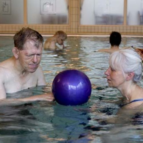 En eldre mann og en eldre dame leker med en ball i et svømmebaseng. Foto.